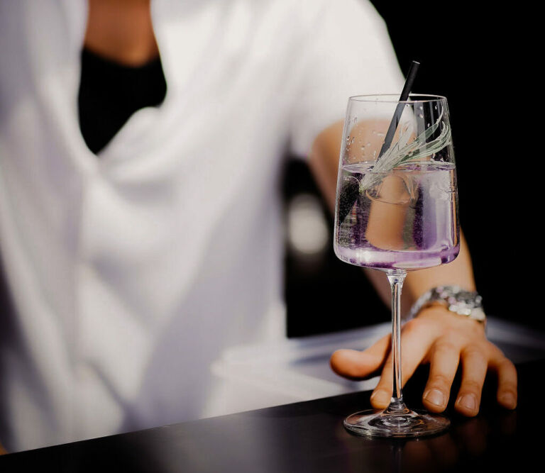 Barkeeper serviert einen stilvoll dekorierten Cocktail in einem Weinglas.