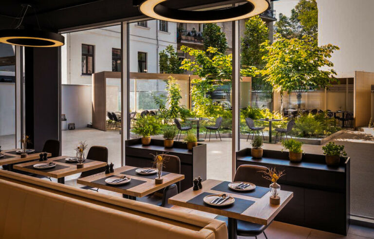 Helles Restaurant mit Blick auf eine grüne Terrasse und modern gedeckten Tischen.